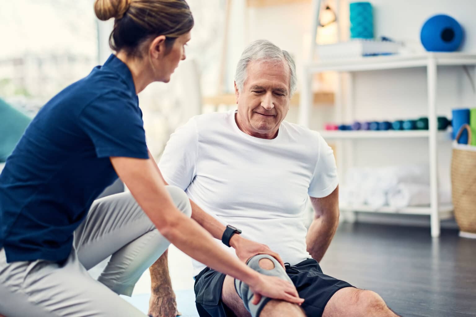 A therapist assisting an elderly man with knee exercises